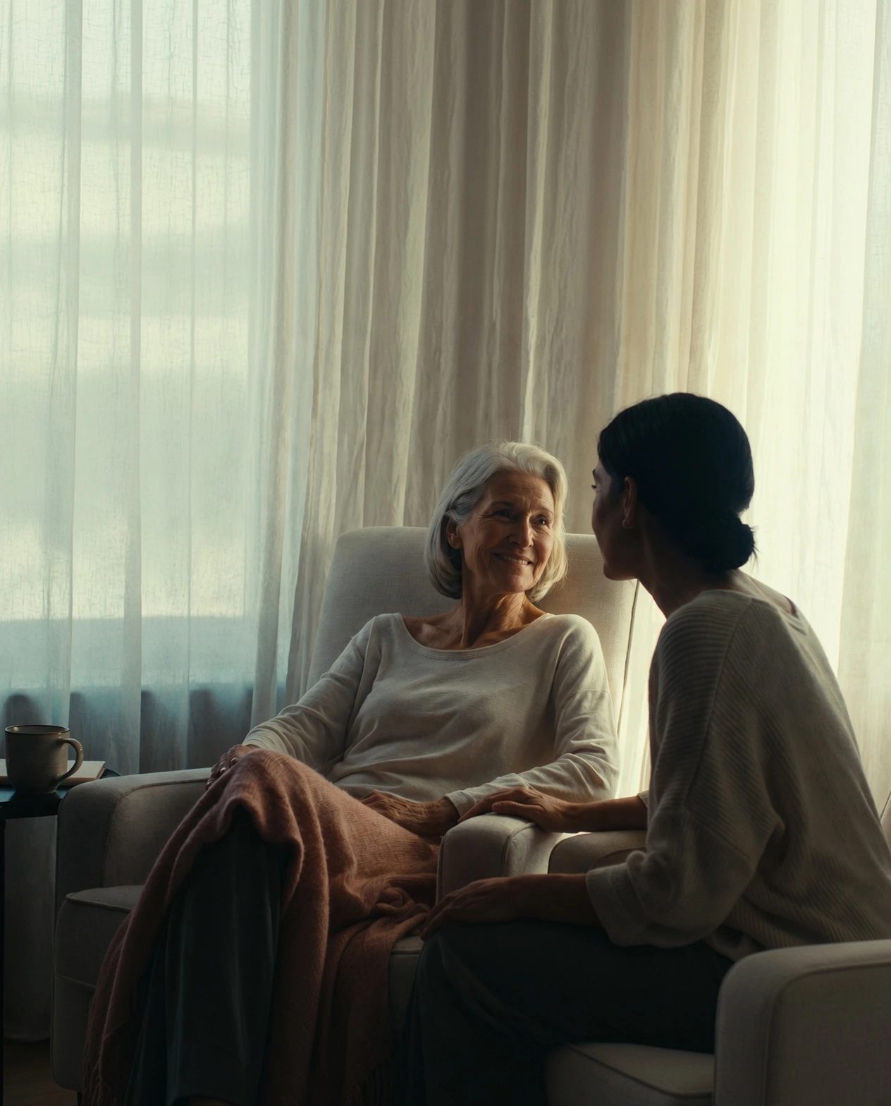 A nurse sitting with an older woman who is resting comfortably in an armchair at home